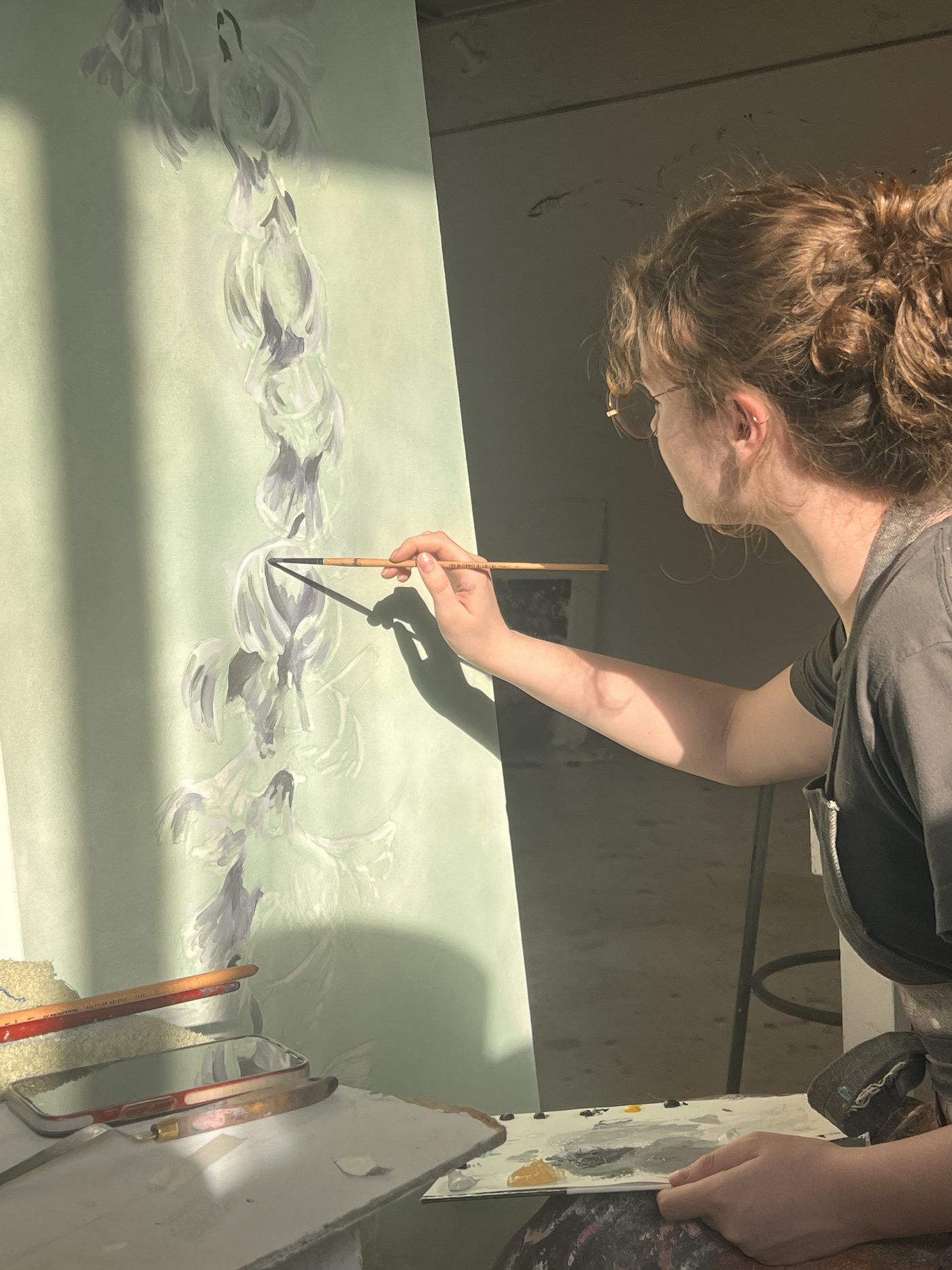Esmée Peets painting a pale green canvas in her studio, in raking sunlight